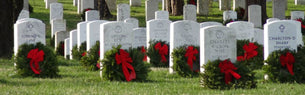 Fresh green wreaths adorned with red ribbons placed against solemn veteran gravestones, symbolizing honor and remembrance at AnchorFinds' Wreaths Across America initiative.